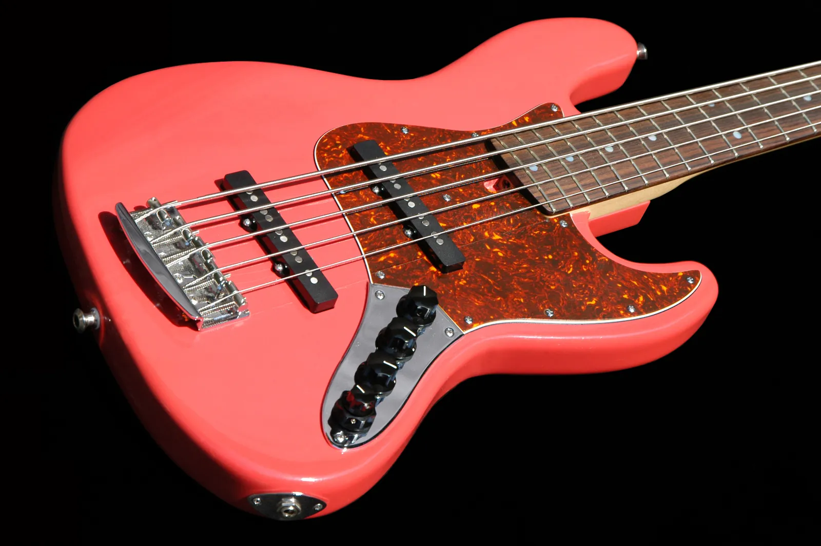 A five-string bass with a coral finish, a tortoiseshell pickguard, two pickups and a dark fingerboard, photographed against black.